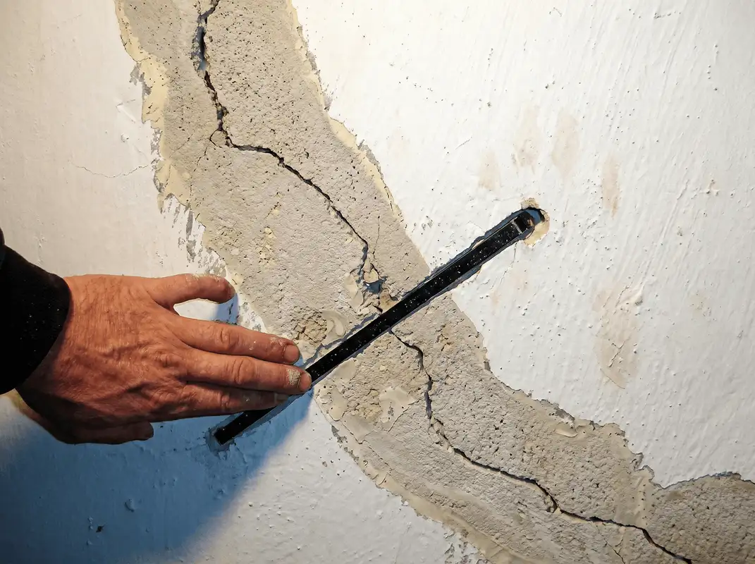 A wall with a large crack is being inspected by a professional in Boston, MA