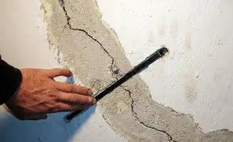A wall with a large crack is being inspected by a professional in Boston, MA